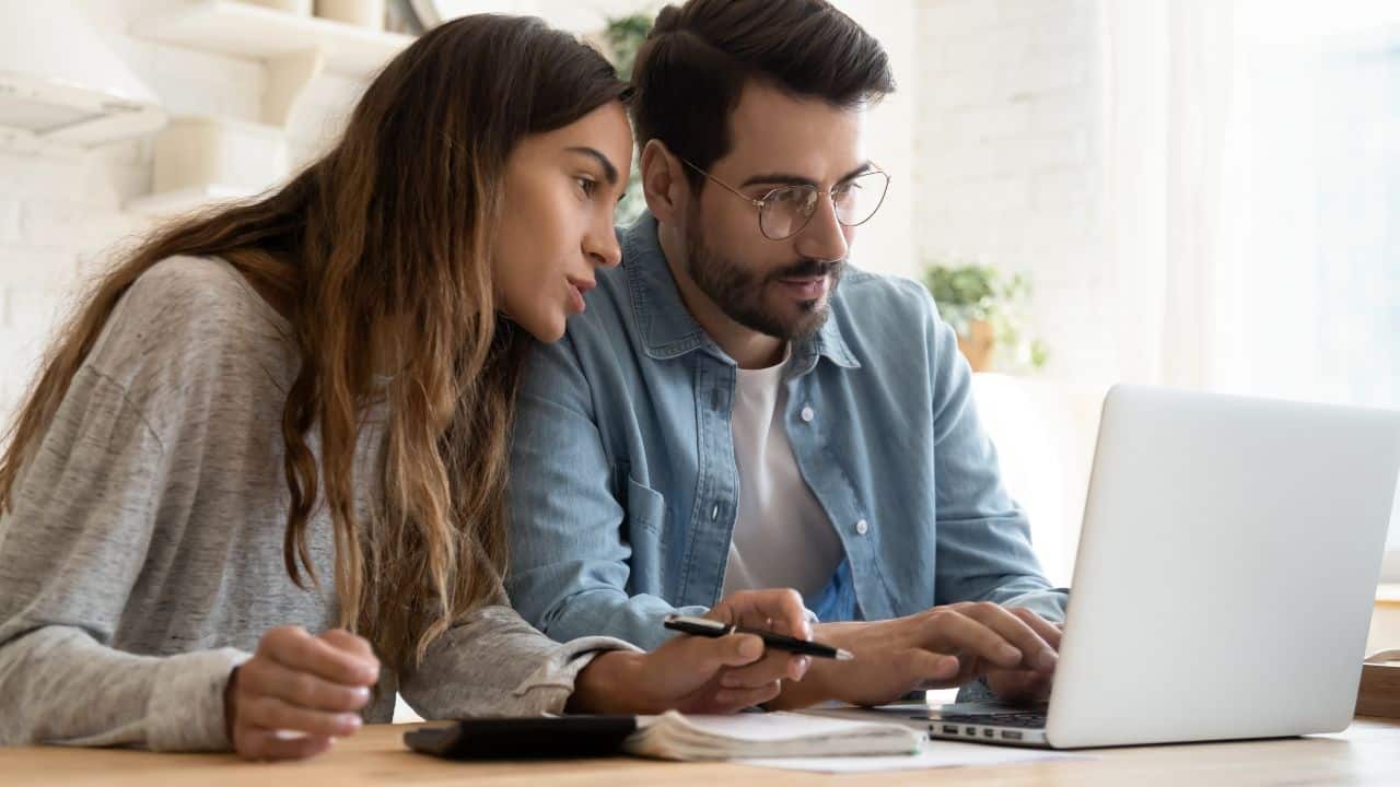 Focused young couple calculating bills, discussing planning budget together, serious wife and husband looking at laptop screen, using online banking services and calculator, checking finances