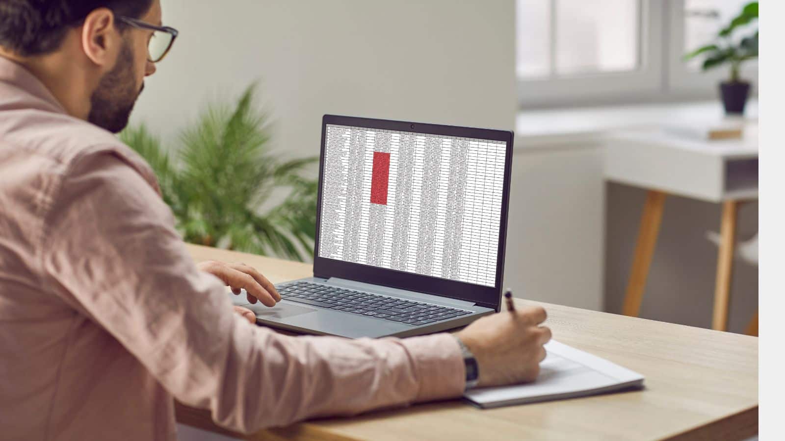 Man writing down something looking at computer spreadsheet