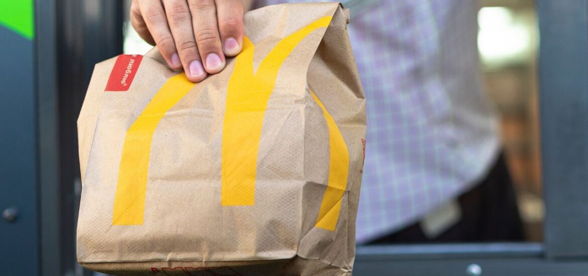 Sankt-Petersburg/Russia - July 21 2019: McDonalds worker holding bag of fast food. Hand with a paper bag through the window of mcdonalds car drive thru service.