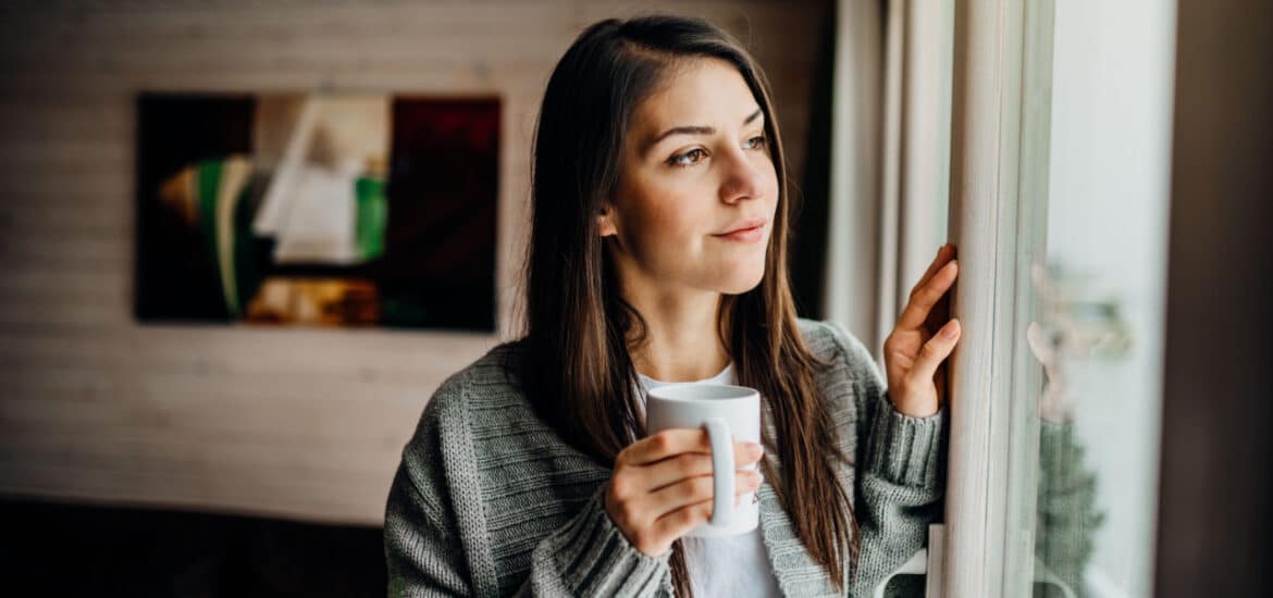 Woman looking out the window with coffee.