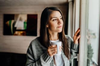 Woman looking out the window with coffee.