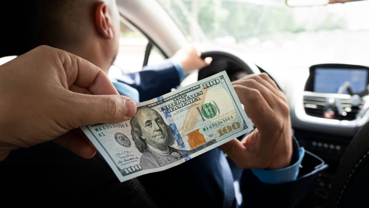 Passenger handing driver a $100 bill.