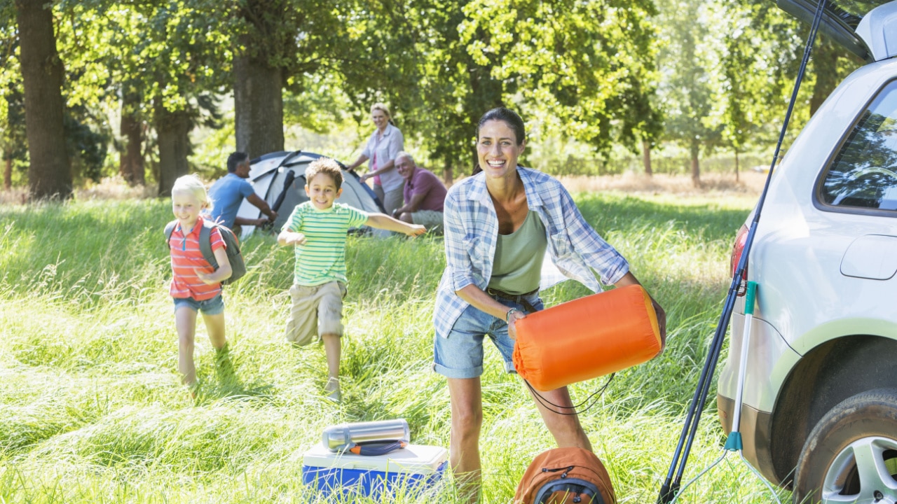 Kids playing and woman unpacking car on family camping trip