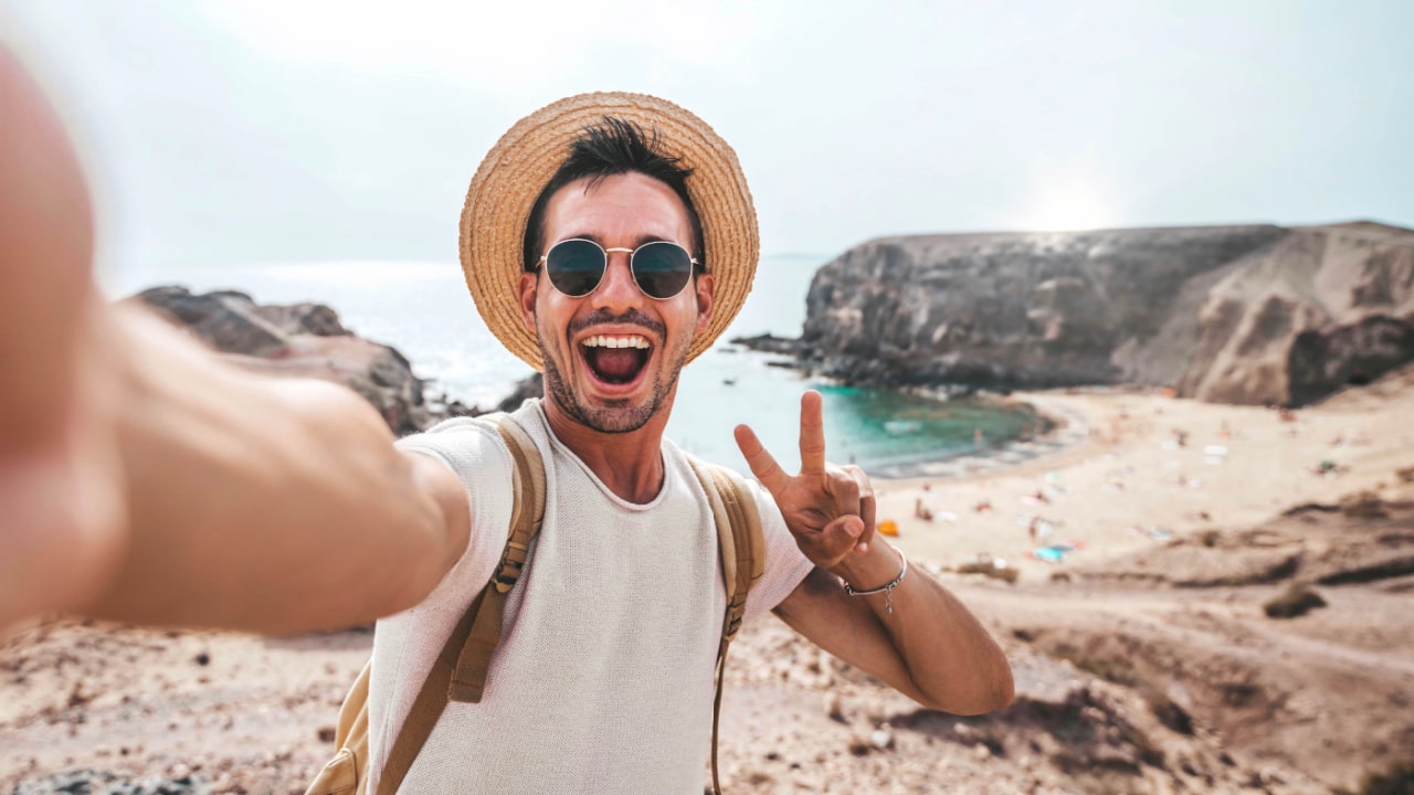 Man on beach with backpack, doing peace sign