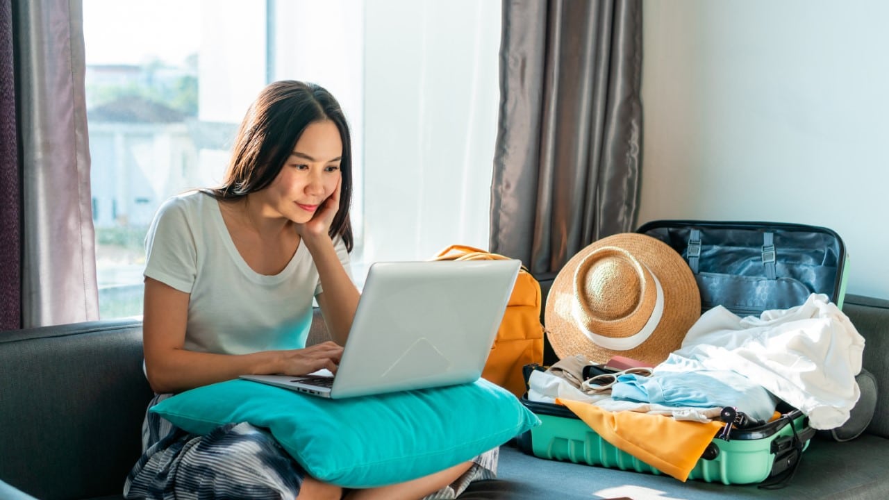 young woman on laptop researching holidays with an open suitcase overflowing