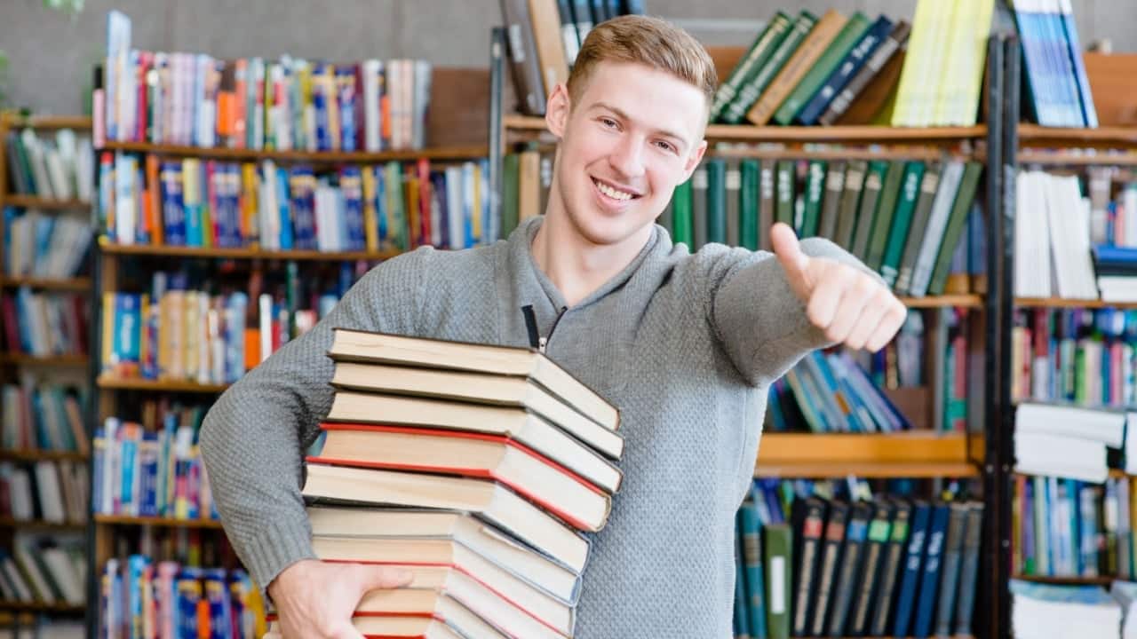 Man holding a stack of books in a library