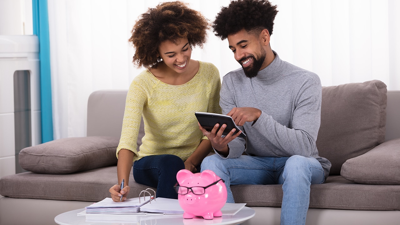 Smiling Young Couple Sitting On Sofa Calculating Invoice