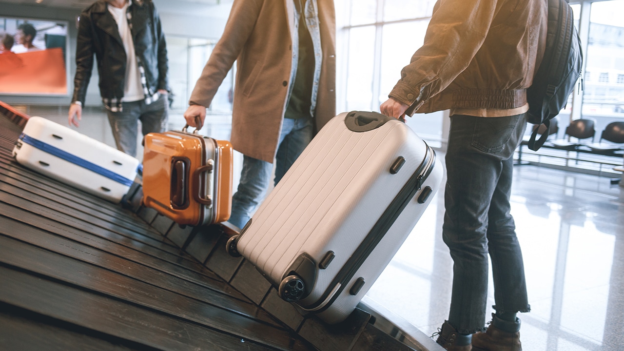 Low angle male friends putting luggages while standing in airport. Journey concept