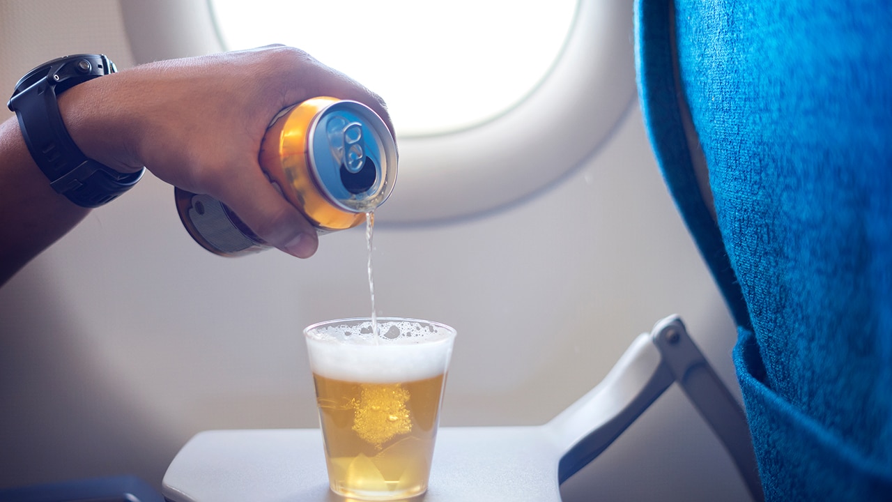 Male hand pouring beer into a plastic glass and making too much foam head on the airplane. Happy man drinking beer on airplane.