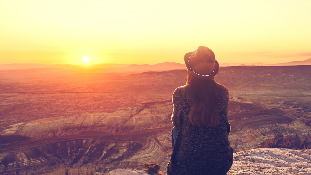 A girl in a hat on top of a hill in silence and loneliness admires a tranquil natural landscape in search of a soul.