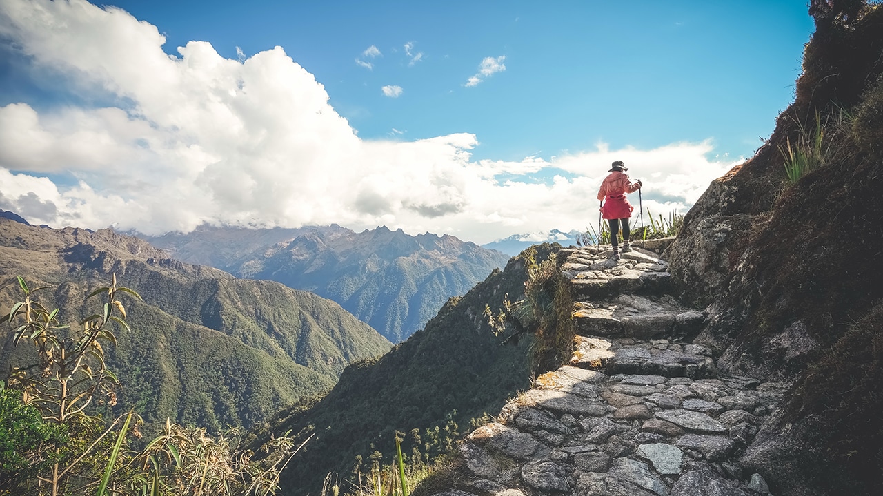 A female hiker is walking on the famous Inca trail of Peru with walking sticks. She is on the way to Machu Picchu.