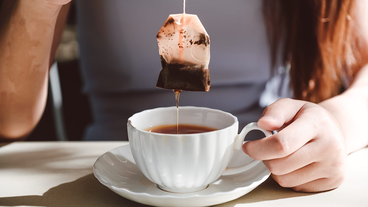 Woman with grey dress is soaking tea bag on vintage white cup, preparing hot tea.Dipping teabag on cup.