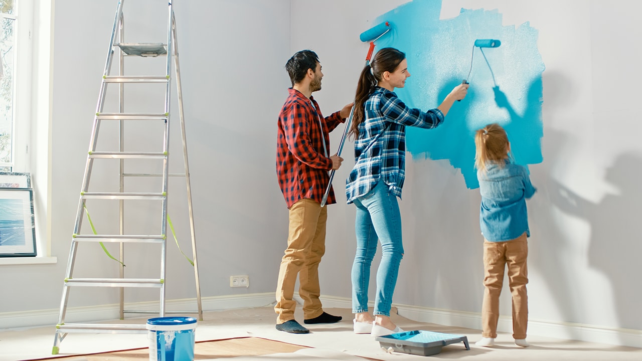 Family Time Together with Small Daughter. Young Father and Mother Showing Their Child How to Paint a Wall with a Roller. Paint Color is Light Blue. Room at Home is Prepared for Renovations.