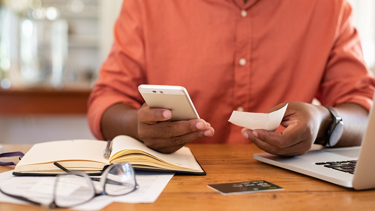 Closeup of african man hands using phone to calculate expenses. Man checking invoice balance on mobile phone app. Close up hands of black guy looking his budget and calculating credit card bills.