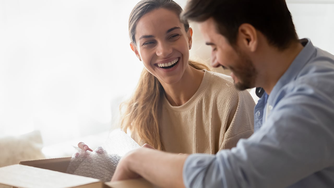 Excited young married couple homeowners chatting, unpacking belongings after moving in new house apartment. Happy family spouses unboxing.