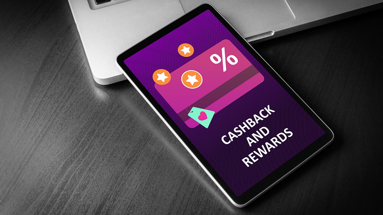 Cashback and Rewards - loyalty program and retail customer money refund service concept. Tablet PC lying on a wooden table with cashback discount card and rewarding marketing points on the screen