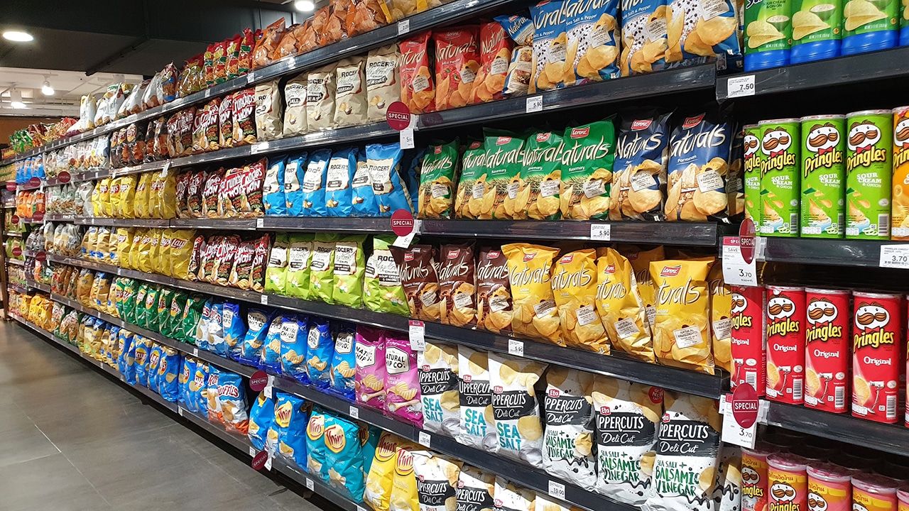 Various brands of chips and snacks on store shelf in grocery store.