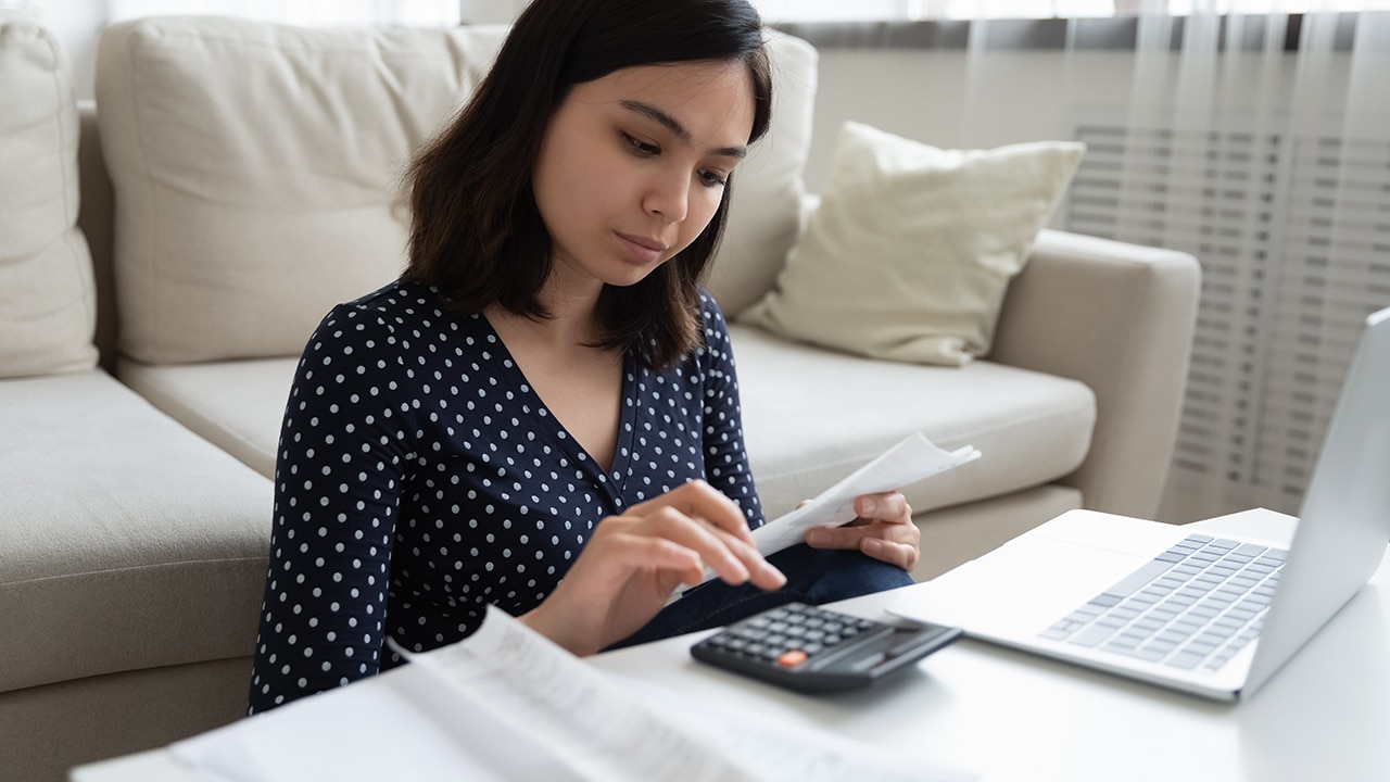 Concentrated millennial vietnamese female engaged in home banking using calculator and laptop. Attentive asian woman count taxes rental tenancy sum to pay online control accounts review utility bills