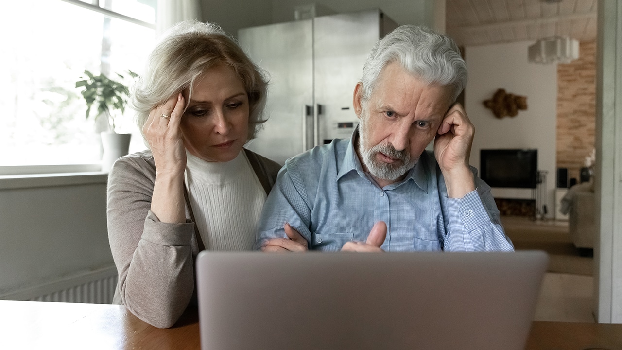 Upset 60s senior couple getting shocking bad news, using laptop together at home, reading email message or talking via video call. Frustrated elder retired husband and wife looking at computer screen
