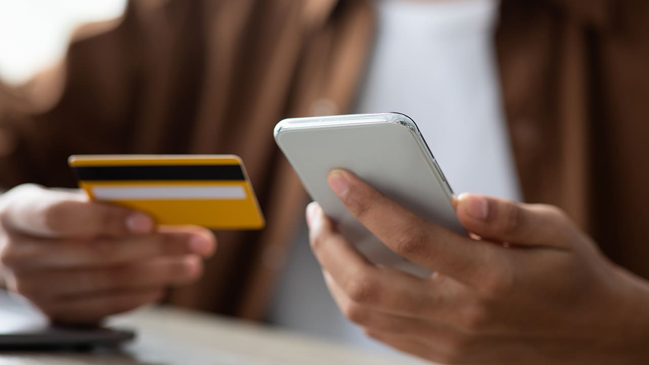 Unrecognizable guy holding credit card and smartphone, purchasing online, paying for services via financial or banking mobile application, closeup. Online payment, e-commerce concept