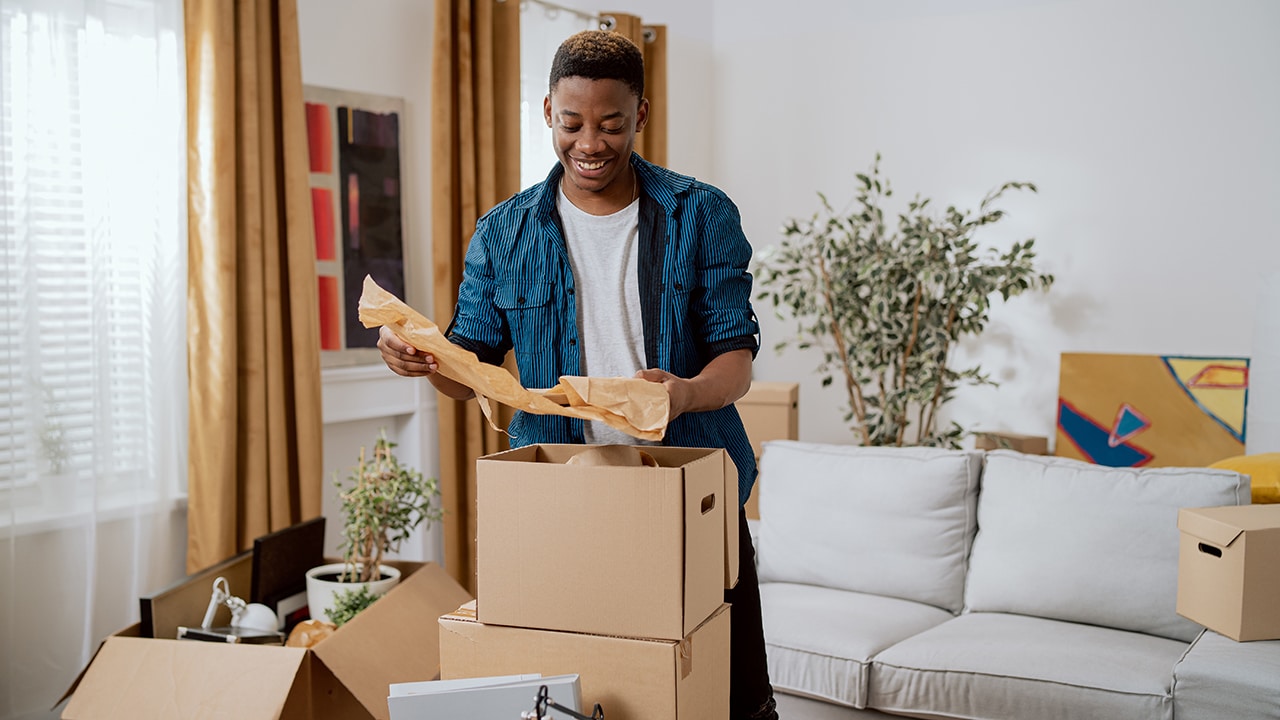 Unpacking cardboard boxes after moving, man cleans new apartment cluttered with things from previous home, looks at items, planning decorations, living room furnishings