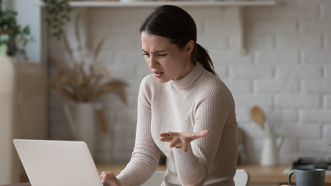 Irritated woman sit at table staring at laptop screen feels angry and confused having problems with broken computer, reading message with bad news in email, lost information, apps malfunction concept