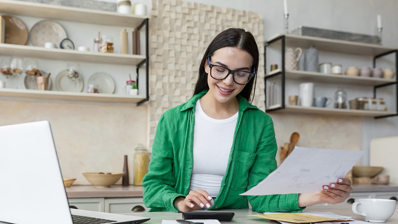 Smiling young beautiful woman reading banking paper notification about last mortgage payment while calculating budget at home. Happy millennial girl feeling excited of good news in letter notice.