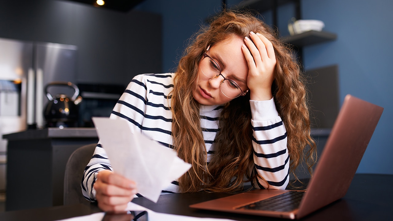Unhappy woman calculates expenses on bills, upset about increased utilities prices. Female counting paychecks, debts, loans, reciepts to pay taxes. Inflation, financial crisis, low paying capacity.
