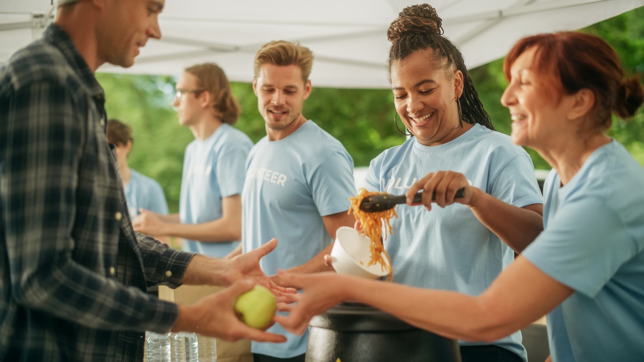 The Concept of Giving: Homeless People Reach Out To Free Volunteer Meals from Multiethnic Team of Volunteers. Humanitarian Aid Charity Workers Serve Meals to People in Need.