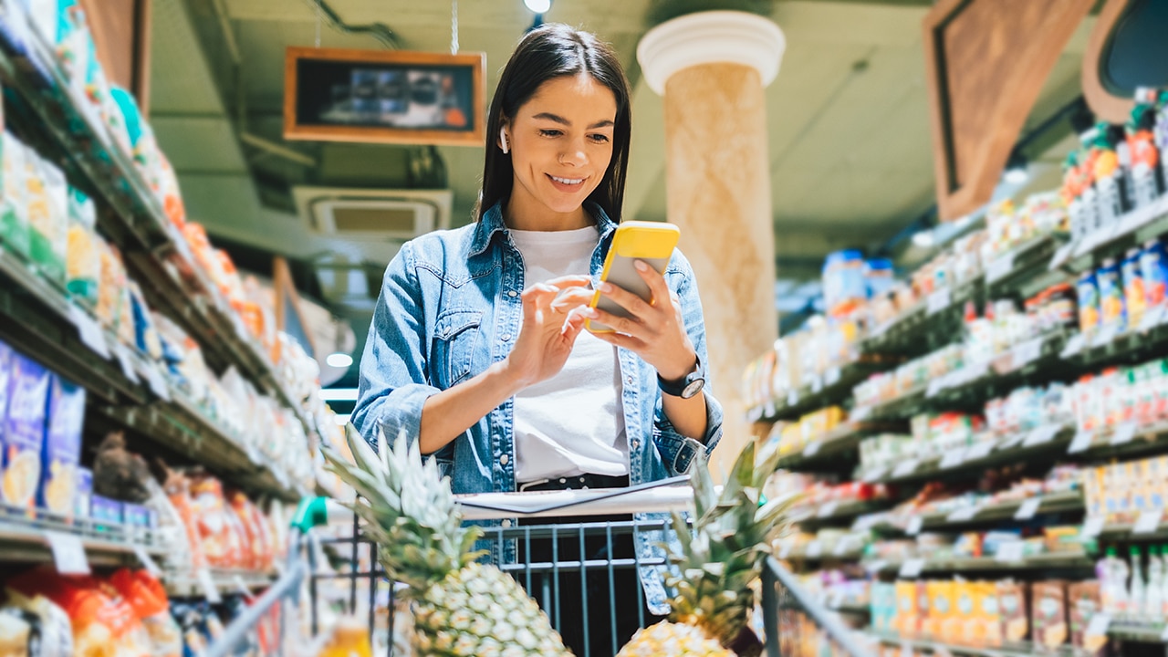 Happy young woman wearing earphones to listen to music in grocery