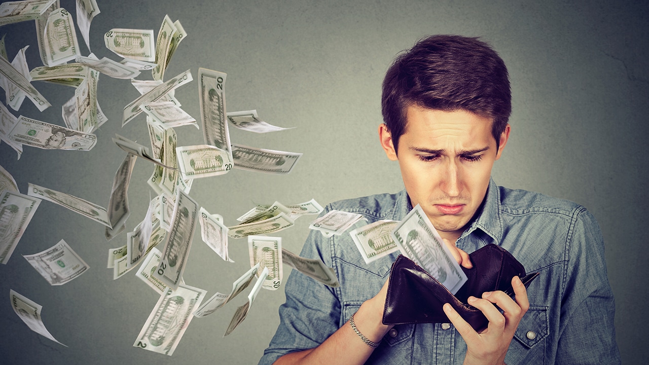 Sad man looking at his wallet with money dollar banknotes flying out away