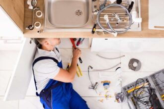 High Angle View Of Male Plumber In Overall Fixing Sink Pipe