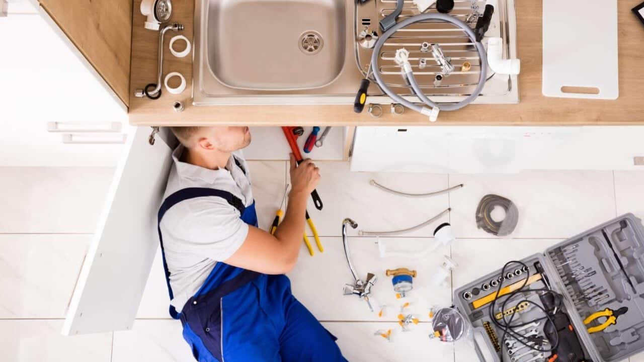 High Angle View Of Male Plumber In Overall Fixing Sink Pipe