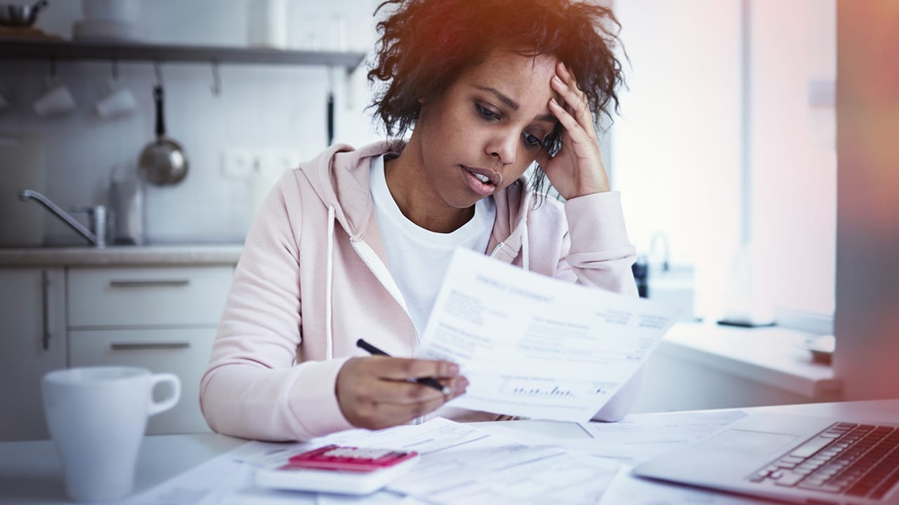Young upset female sitting at kitchen table with laptop, dealing with financial stress, feeling pressure because of mortgage debt, worrying a lot or feeling anxious over money