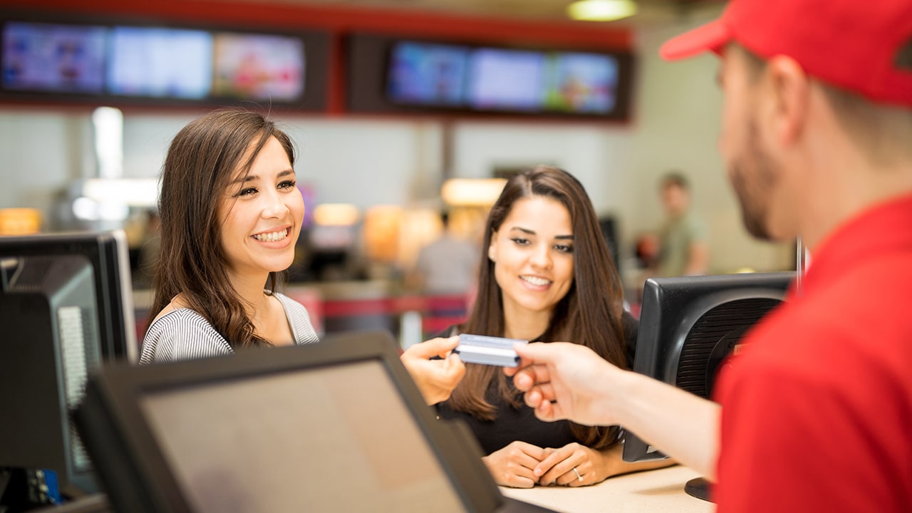 Point of view of a male worker getting a credit card from a pair of friends at the movie theater