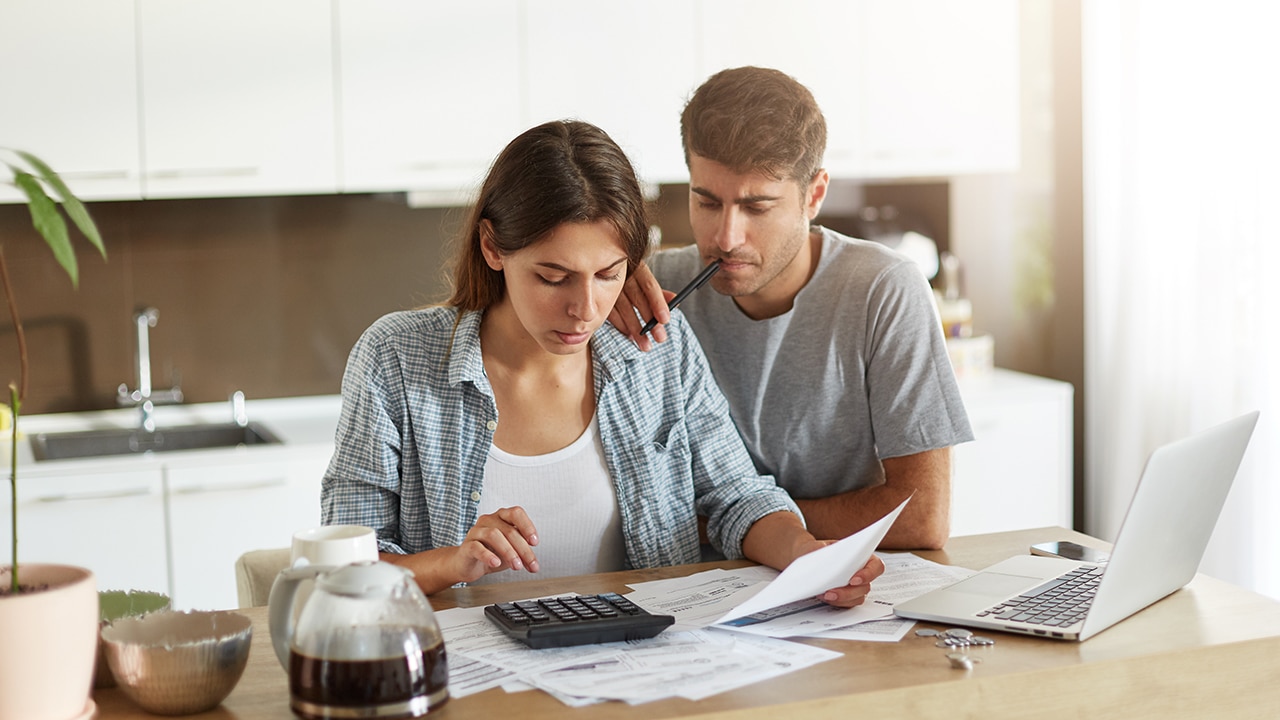 Young couple calculating all their expenses,Preoccupied man holding pen leaning at shoulder of her wife, looking in paper