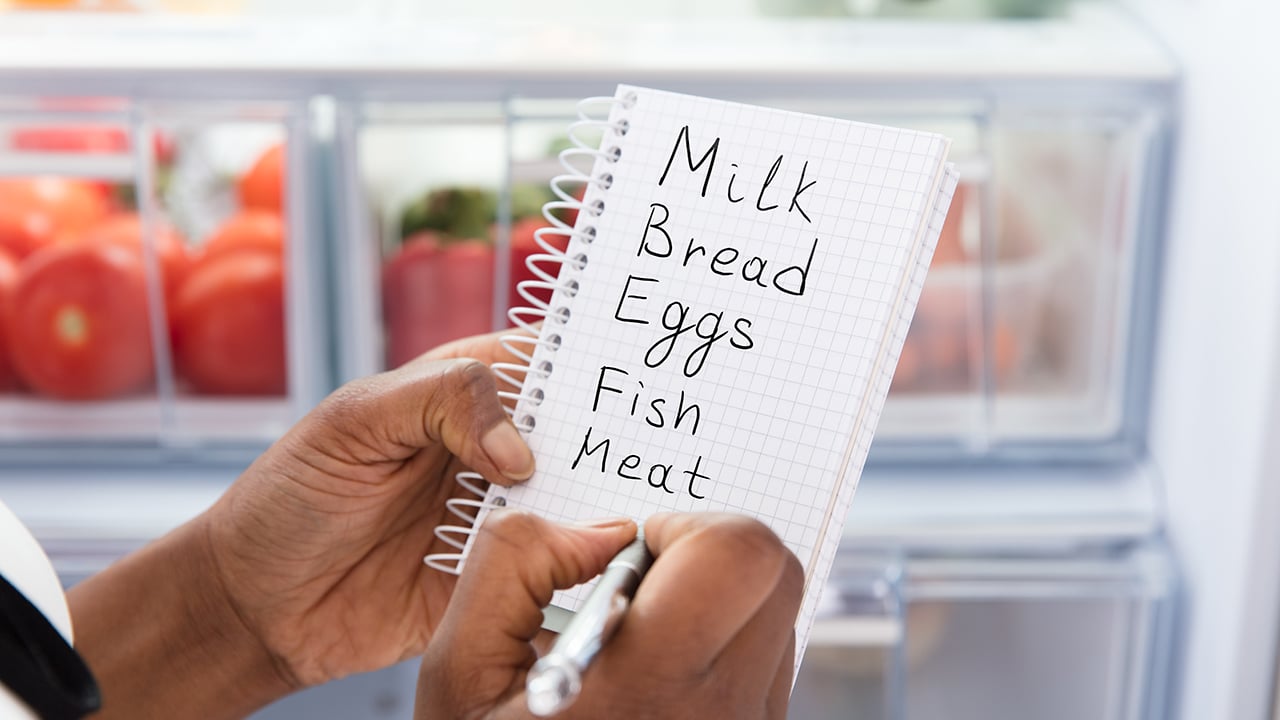 Close-up Of Young African Woman Writing Shopping List Near Open Refrigerator