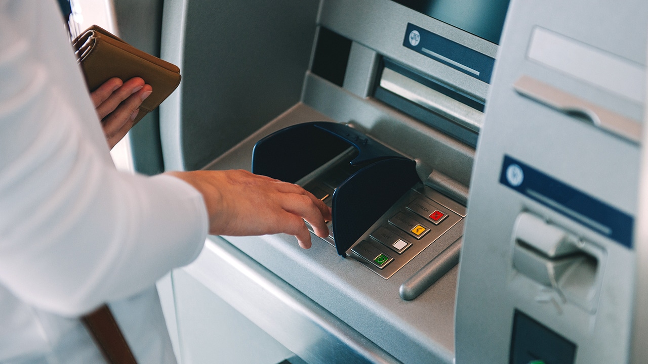 Woman using ATM holding wallet an pressing the PIN security number on the keyboard automatic teller machine