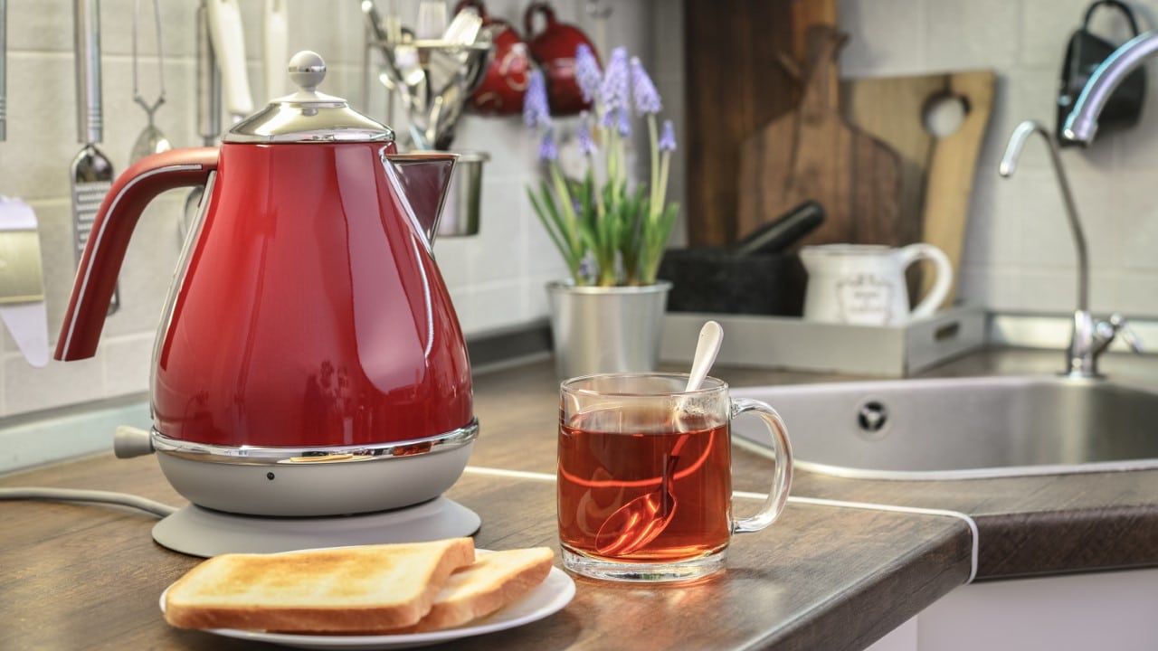 Red electric kettle in retro slile with bread and cap of tea in kitchen interior closeup