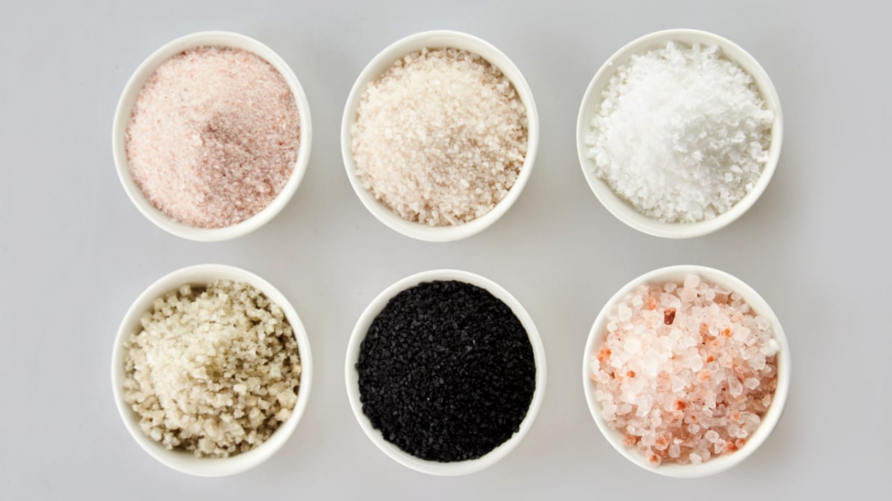 Six assorted gourmet salts in bowls with black Hawaiian lava salt, Indus salt, Fleur de sel, rock salt and sea salt viewed from above