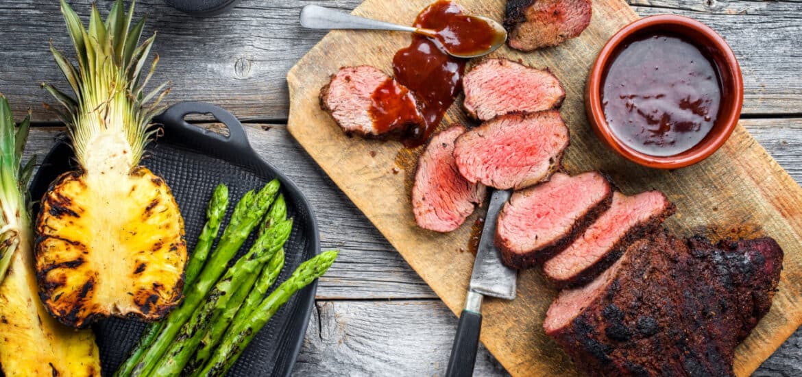 Barbecue dry aged wagyu tri tip steak with grilled pineapples and green asparagus top view on a wooden cutting board