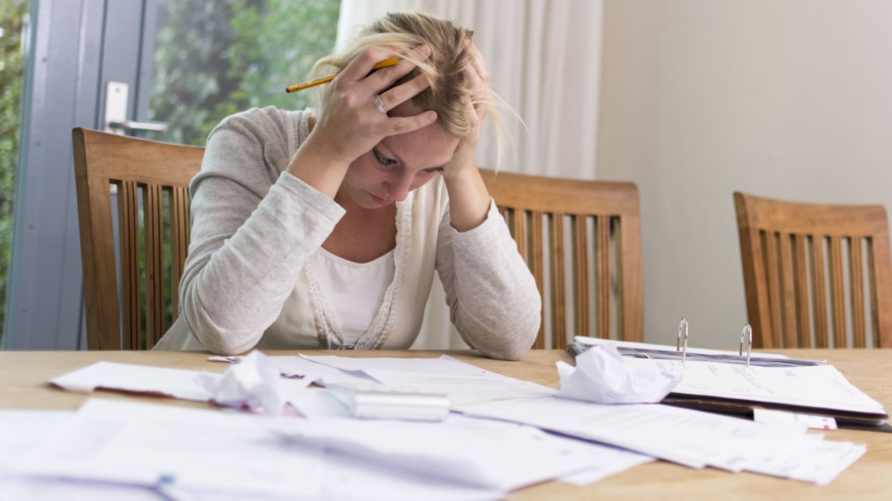 worried woman with head in hands sitting at a desk covered in documents