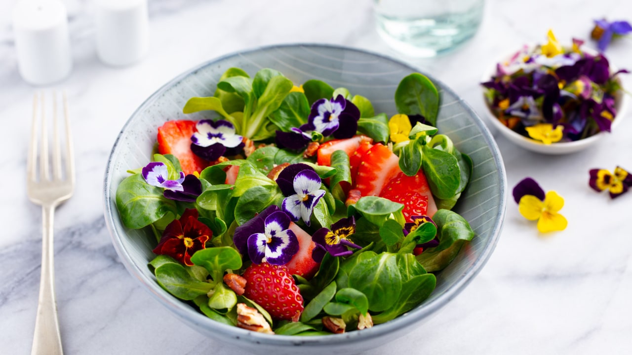 Fresh green salad with strawberries and edible flowers in a bowl.