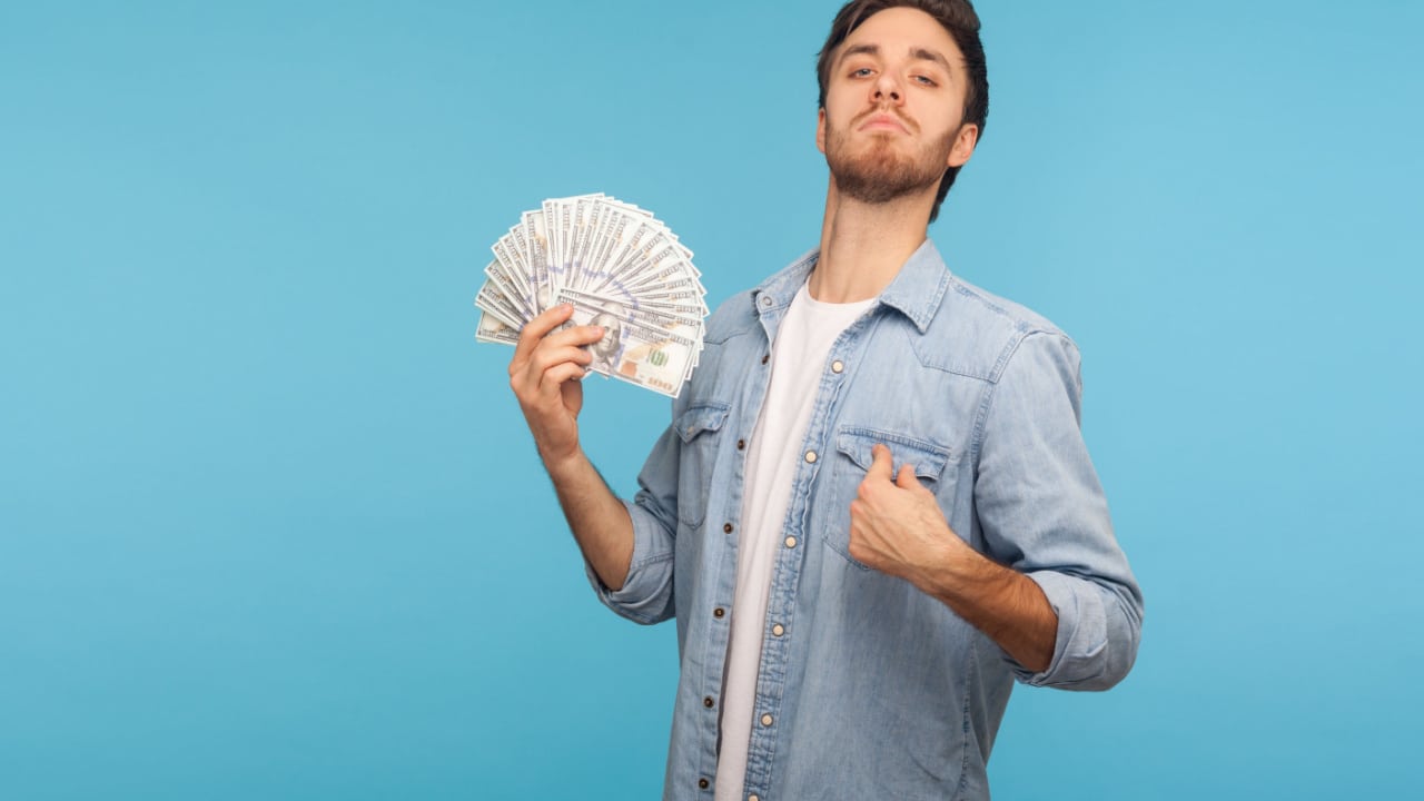 man holding a wad of cash and ponting at himself