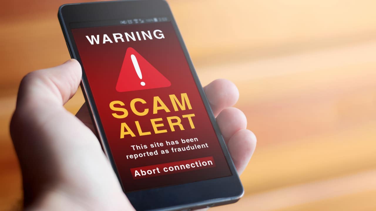 mobile phone in a person's hand showing a warning message about a potential scam