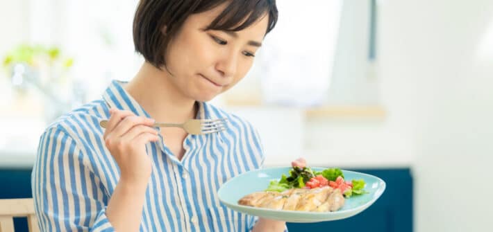 Woman looking unsure at a plate of healthy food.