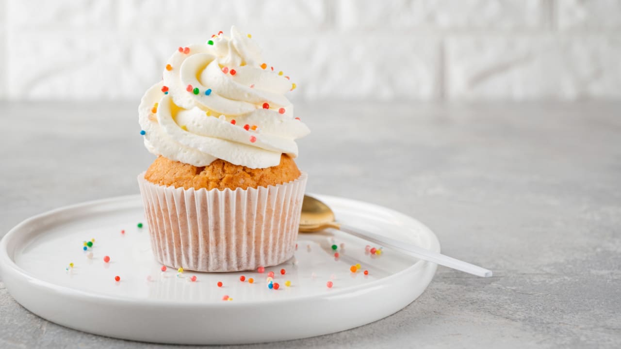 Delicious vanilla cupcakes with cream cheese and sugar candy on a gray background.