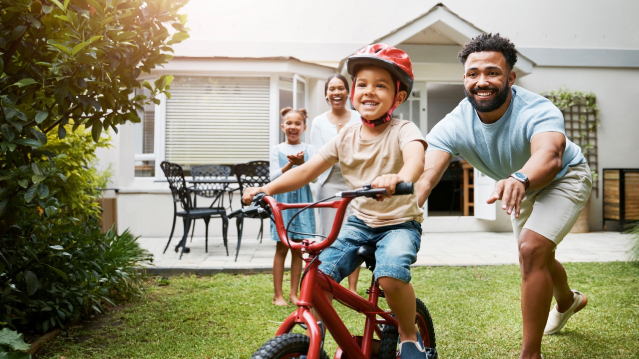 family playing in the garden with a young boy on a bicycle wearing a helmet