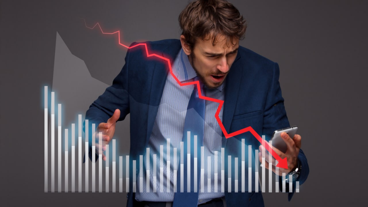 man holding a mobile phone with an image of investment charts showing a downward trending market