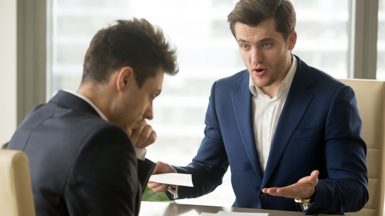 one man with a document in his hand looking frustrated at another man who looks concerned